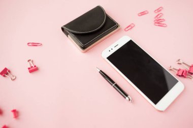Kırtasiye, beyaz akıllı telefon, kalem, cüzdan, saat, takvim, defter. Pembe arka plan.