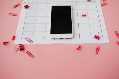 Beyaz akıllı telefon kağıt takvimde yer alır. Pembe arka plan.