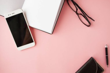 Kırtasiye, beyaz akıllı telefon, Gözlük, kalem, cüzdan, saat, takvim, defter. Pembe arka plan.