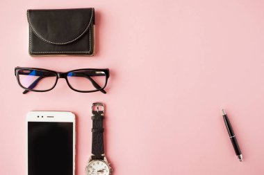 Kırtasiye, beyaz akıllı telefon, Gözlük, kalem, cüzdan, saat, takvim, defter. Pembe arka plan.