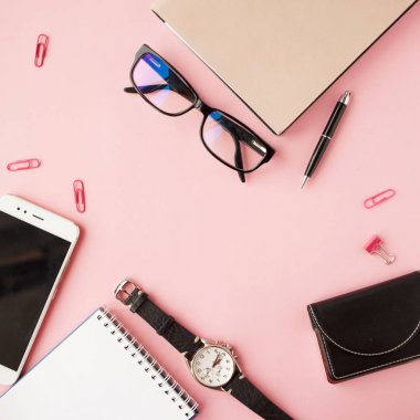 Kırtasiye, beyaz akıllı telefon, Gözlük, kalem, cüzdan, saat, takvim, defter. Pembe arka plan.