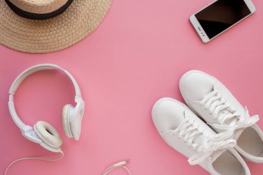 Beyaz spor ayakkabılar, hasır şapka, kulaklıklar, akıllı telefon parlak pembe bir arka plan üzerinde yatıyor.
