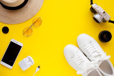 Beyaz spor ayakkabılar, şapka, güneş gözlükleri, kablosuz kulaklıklar, akıllı telefon ve fotoğraf makinesi ayellow arka planda yatıyor.
