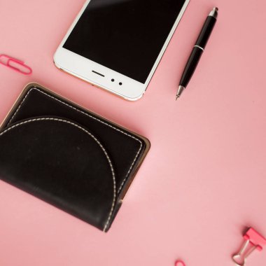 Kırtasiye, beyaz akıllı telefon, kalem, cüzdan, saat, takvim, defter. Pembe arka plan.