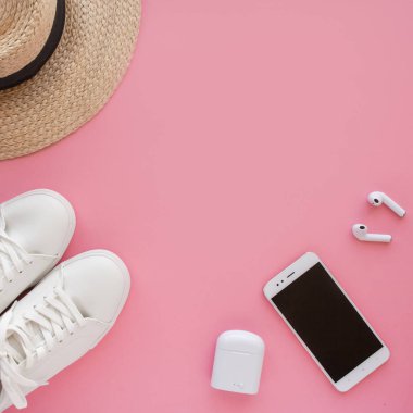 Beyaz spor ayakkabılar, şapka, kablosuz kulaklık, akıllı telefon parlak pembe bir arka planda yatıyor..