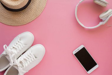 Beyaz spor ayakkabılar, hasır şapka, kulaklıklar, akıllı telefon parlak pembe bir arka plan üzerinde yatıyor.