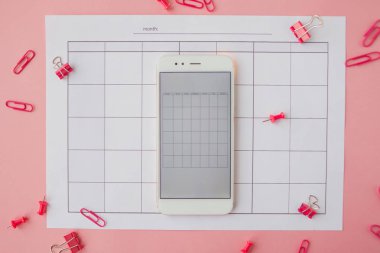 Beyaz akıllı telefon kağıt takvimde yer alır. Pembe arka plan.