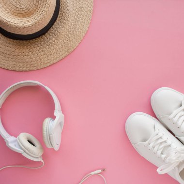 Beyaz spor ayakkabılar, hasır şapka, kulaklıklar, parlak pembe bir arka plan üzerinde yatıyor.