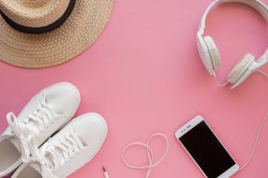 Beyaz spor ayakkabılar, hasır şapka, kulaklıklar, akıllı telefon parlak pembe bir arka plan üzerinde yatıyor.