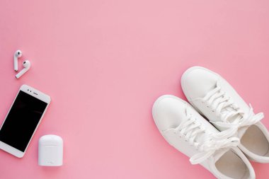 Beyaz hapşırlar, kablosuz kulaklıklar ve akıllı telefon pembe bir arka plan üzerinde yatıyor.