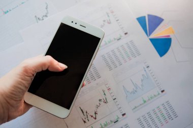 Finansal raporların arka planında boş ekrana sahip akıllı telefon