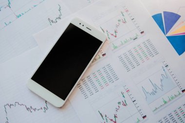 Finansal raporların arka planında boş ekrana sahip akıllı telefon