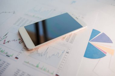 Finansal raporların arka planında boş ekrana sahip akıllı telefon