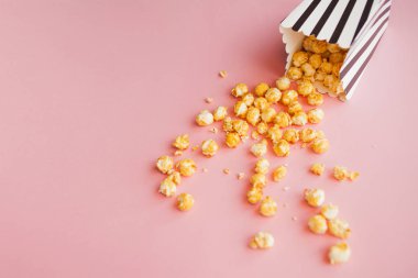 Kağıt torbada Popcorn pembe arka plan üst görünümüne dağılmış