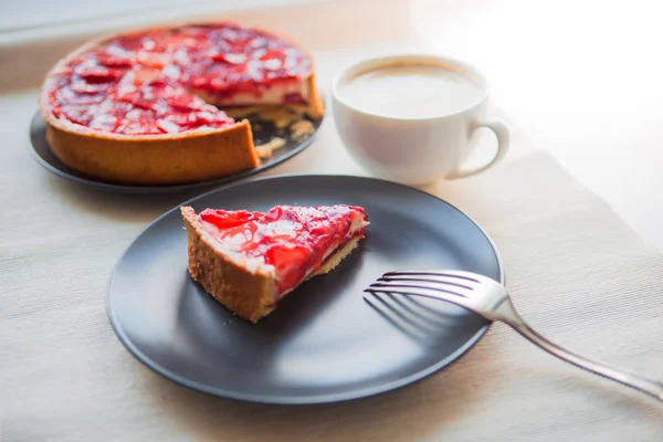 Bodegón con una taza de café y postre dulce con fresas, pastel de queso con rodajas de bayas en gelatina en la parte superior . — Foto de Stock