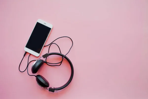 De muziek in de smartphone en hoofdtelefoon op een roze achtergrond. — Stockfoto