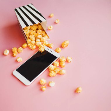Film ve seri abonelik, konsept. akıllı telefon bir siyah ve beyaz biber patlamış mısır çizgili kutu yanında yalan