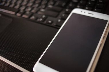 Dizüstü Klavye yanında boş bir siyah ekran ile akıllı telefon. Kopya alanı, siyah arka plan.