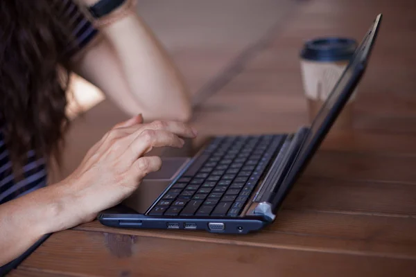 Neat young female hands with a modest manicure, with large wrist watches, work at a laptop, standing on a wooden table.