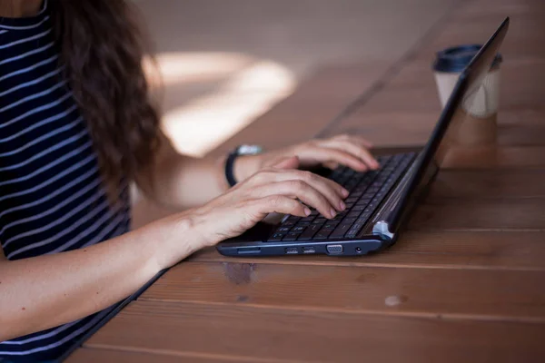 Neat young female hands without manicure, with large wrist watches, work at a laptop, standing on a wooden table.