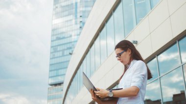 İş merkezinin arka planda elinde bir dizüstü bilgisayar ile genç hırslı kadın.
