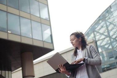 Kariyer gelişimi ve hırsları, kavram. İş merkezinin arka planında elinde dizüstü bilgisayar olan genç iş kadını.
