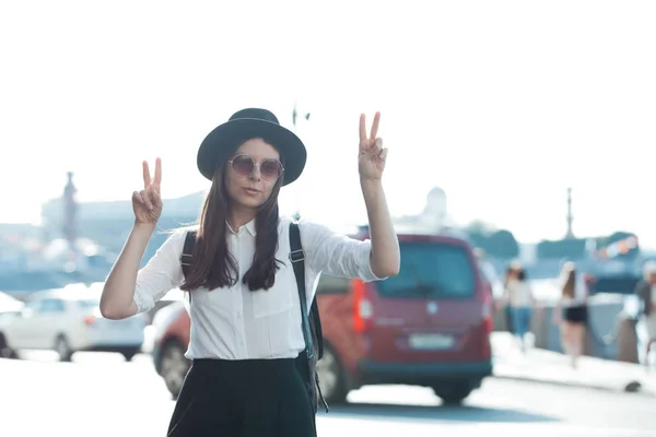 Mujer joven en sombrero y gafas de sol redondas caminando en la ciudad. Chica turística disfruta de la caminata . —  Fotos de Stock