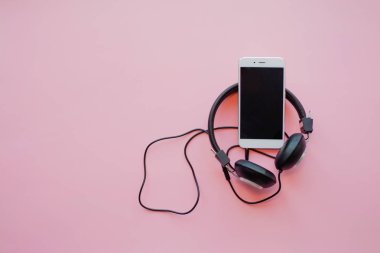 Pembe arka planda akıllı telefon ve kulaklıkta müzik.