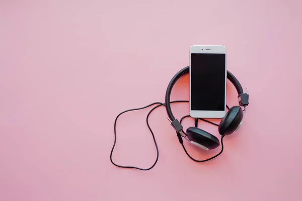 De muziek in de smartphone en hoofdtelefoon op een roze achtergrond. — Stockfoto