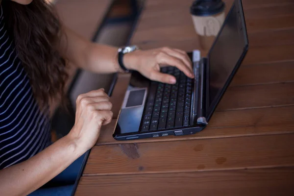 Neat young female hands without manicure, with large wrist watches, work at a laptop, standing on a wooden table.