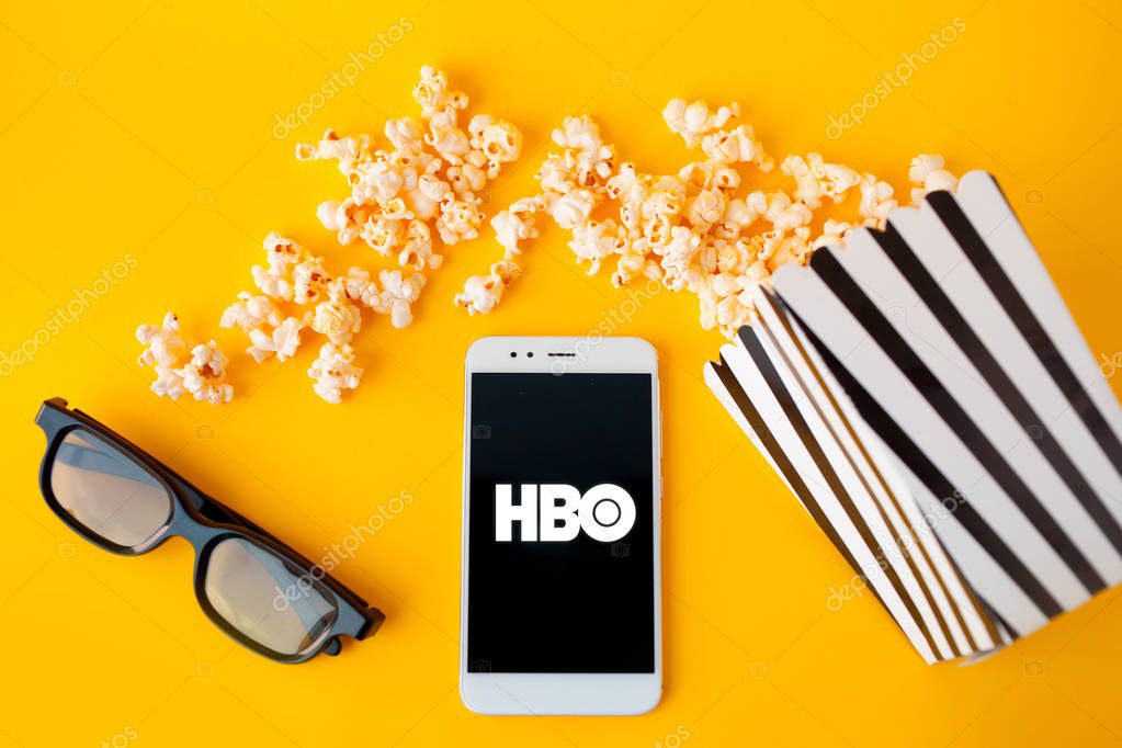 SAINT PETERSBURG, RUSSIA - JULY 7, 2019: Movies and series by subscription, concept. smartphone with HBO logo lie next to a black and white papper striped box of popcorn. illustrative editorial