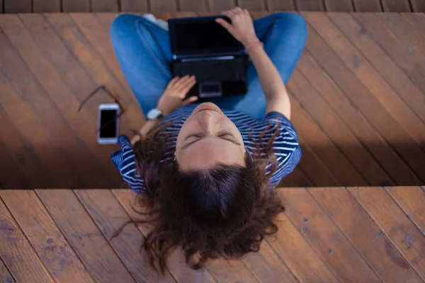 Egy barna lány ül lába keresztbe egy padon, egy laptop az ölében, az arca emelkedik fel, a szeme zárva. — Stock Fotó