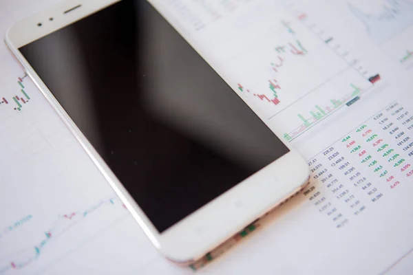 Смартфон с пустым экраном на фоне финансовых отчетов — стоковое фото