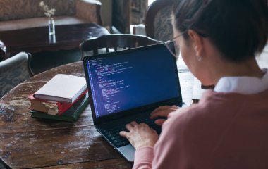 Hack sistemi. Koyu saçlı ve pembe kazak ve gözlük ile Heyecanlı kız bir kütüphanede bir dizüstü bilgisayarda kod yazıyor.