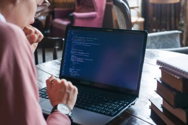 Hack sistemi. Koyu saçlı ve pembe kazak ve gözlük ile Heyecanlı kız bir kütüphanede bir dizüstü bilgisayarda kod yazıyor.