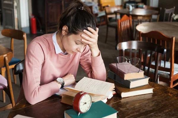 Falta de sono. Estudante, morena, curvada sobre livros em uma mesa em uma biblioteca antiga, apoiando a cabeça com a mão . — Fotografia de Stock