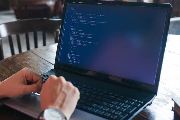 Neat hands lie on the keyboard of a laptop standing on an old desk in the library. On the monitor site code.