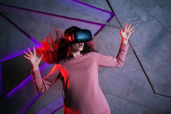 Watch out. Young woman with vr glasses and fluttering hair actively reacts, is afraid of what is happening in the game.