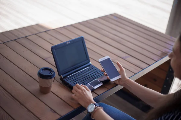 Neat young female hands with a modest manicure, with large wrist watches, work at a laptop, standing on a wooden table.