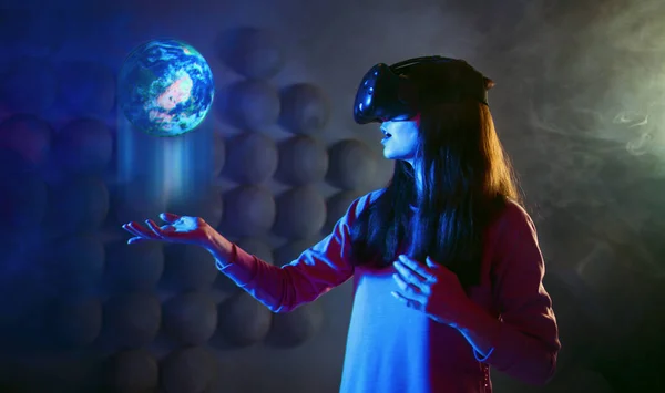 O futuro está nas tuas mãos. Uma mulher encantada com óculos de realidade virtual detém projeção holográfica do planeta . — Fotografia de Stock