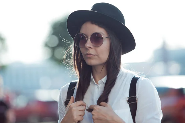 Young woman in hat and round sunglasses walking in city. Girl tourist enjoys the walk.