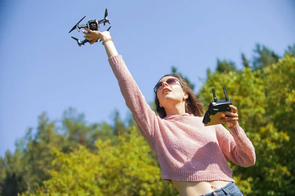 Una joven en el parque lanza, sostiene el dron con su brazo extendido por encima de su cabeza, en otro panel de control . —  Fotos de Stock