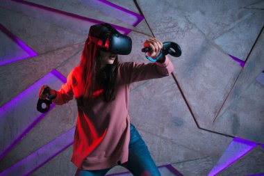 Kılıç kullan. Sanal kasklı genç bir kadın, sanal kılıçların kolları gibi her iki elinde de kontrolörler kullanır..