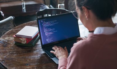 Hack sistemi. Koyu saçlı ve pembe kazak ve gözlük ile Heyecanlı kız bir kütüphanede bir dizüstü bilgisayarda kod yazıyor.