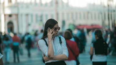 Büyük şehrin sokaklarında kalabalığın içinde olan kız. Şehirde genç bir kadın cep telefonu kullanıyor.