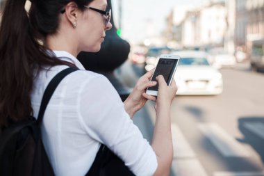 Mobil uygulamayı kullanarak taksi çağırın. Şehirde genç bir kadın elinde bir akıllı telefon ile yolun yanında duruyor