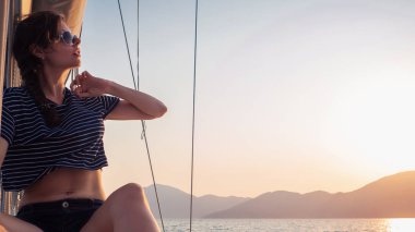 çizgili bir t-shirt çekici genç kadın bir yelkenli yat güvertesinde gün batımı sahiptir. Yelkenli yarış