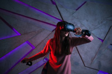 Kılıç kullan. Sanal kasklı genç bir kadın, sanal kılıçların kolları gibi her iki elinde de kontrolörler kullanır..