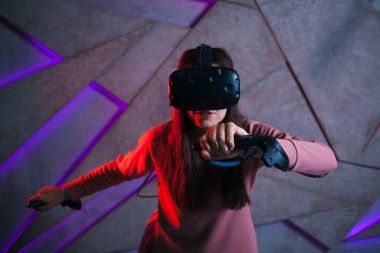 Kılıç kullan. Sanal kasklı genç bir kadın, sanal kılıçların kolları gibi her iki elinde de kontrolörler kullanır..