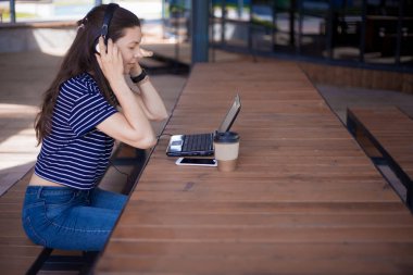 Akıllı telefonu olan bir kız öğrenci, dizüstü bilgisayarda oturur ve kulaklıkla dikkatlice dinler, yabancı dil öğrenir.